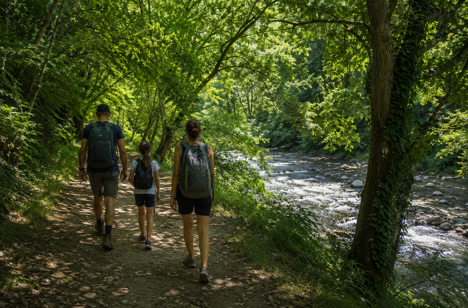 Una famiglia con zaini che percorre a piedi un sentiero ombreggiato lungo il fiume Marecchia, circondata da alberi e natura a inizio estate.